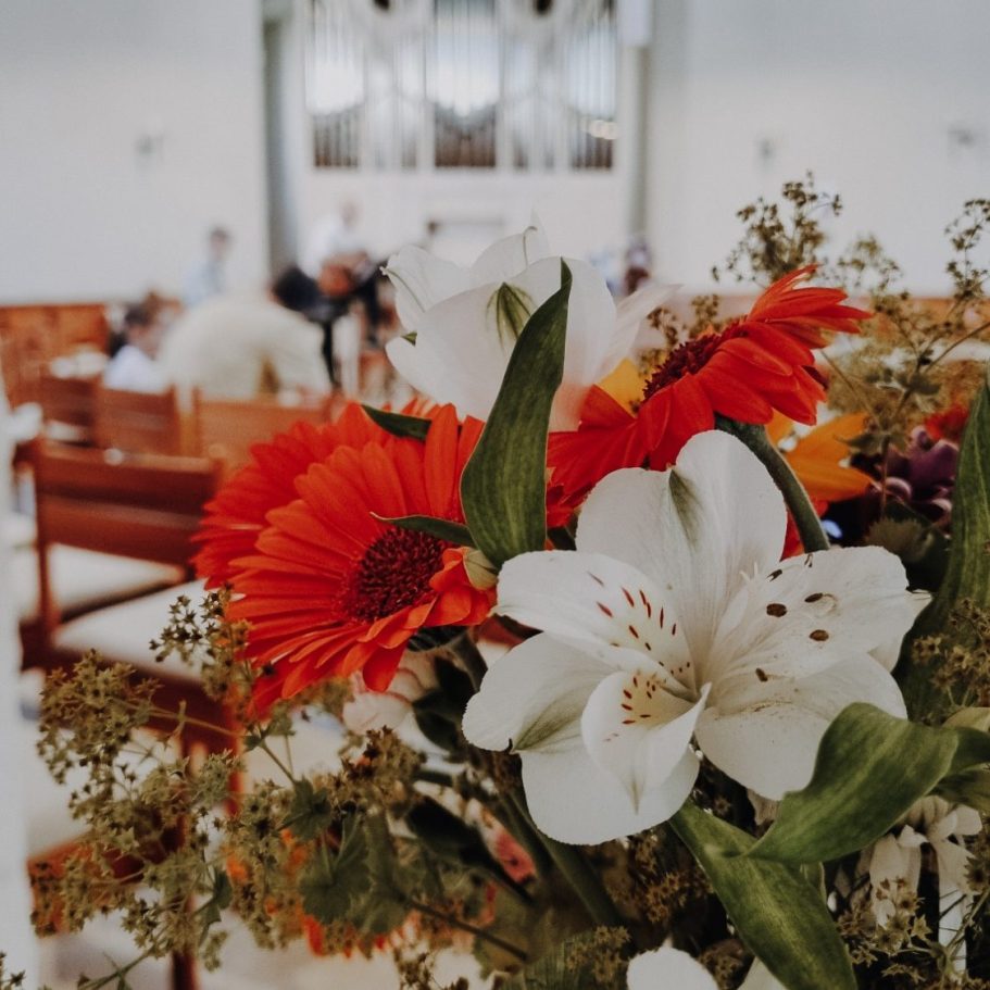 Bunte Blumenarrangement mit roten Sonnenblumen und weißen Lilien in einem Festsaal.