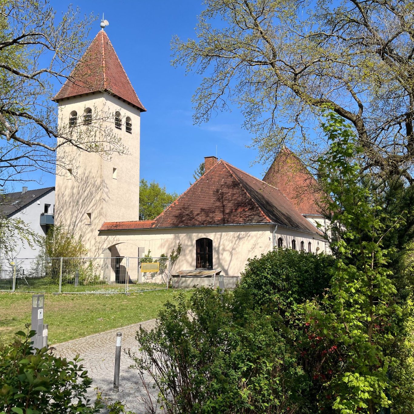 Eine kleine Kirche mit Spitzdach und einem Glockenturm, umgeben von Bäumen und Gras.