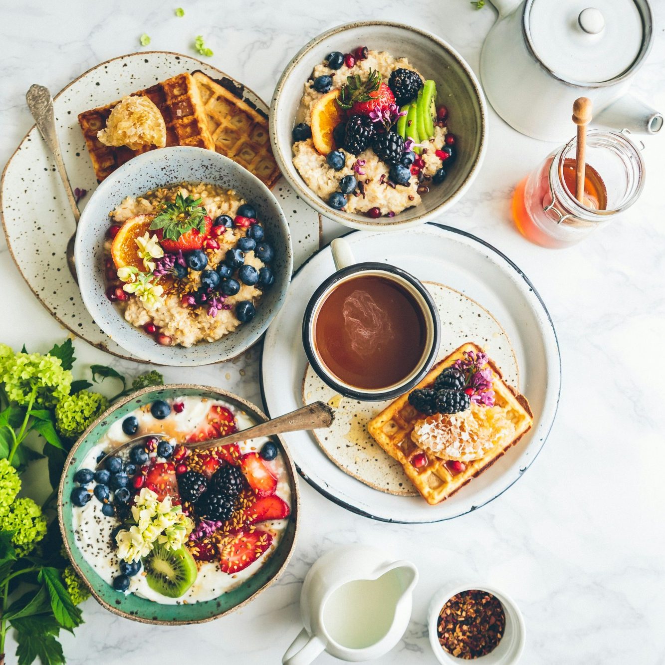 Verschiedene Schalen mit Früchten, Joghurt, Waffeln und einem Getränk auf einem Tisch.
