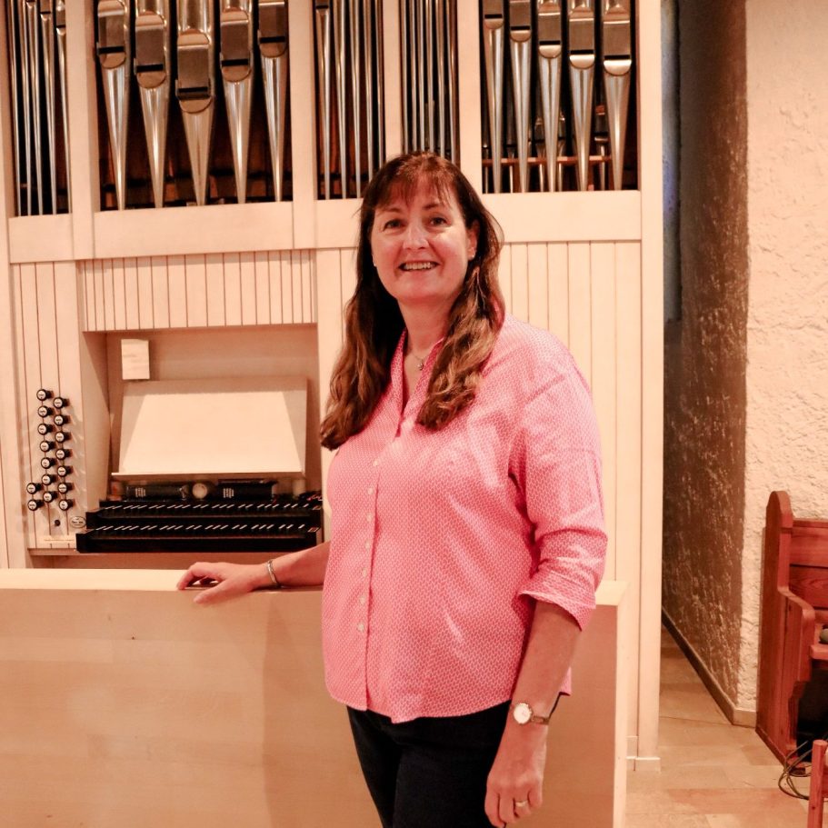 Frau in rosa Hemd steht neben einer Orgel in einem Kirchenraum.