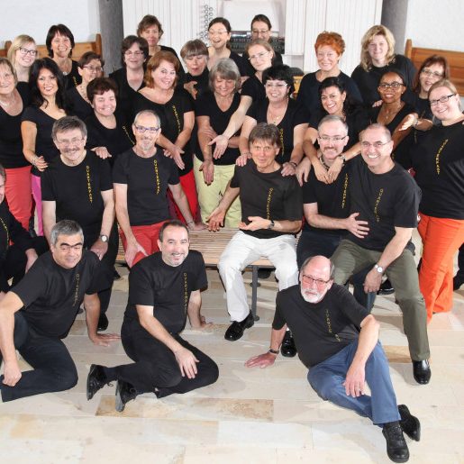 Gruppenfoto von etwa 30 Personen in schwarzen T-Shirts, lächelnd, auf einem hellen Boden.